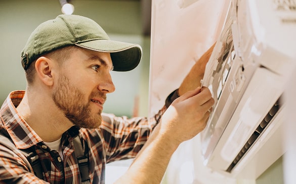 man adjusting home thermostat next to indoor air conditioning unit