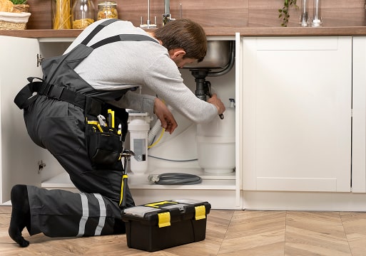 Plumber fixing leaky pipe under a sink